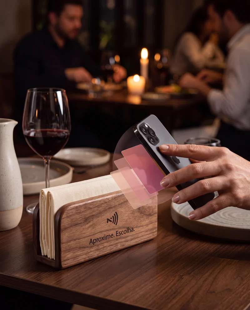 Celular aproximado de uma guardanapeira de madeira com NFC, em uma mesa com vinho